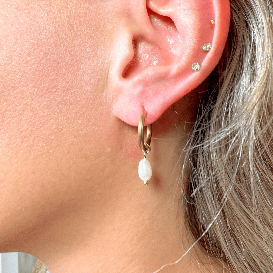 Close-up of an ear wearing a gold hoop earring with a pearl drop.