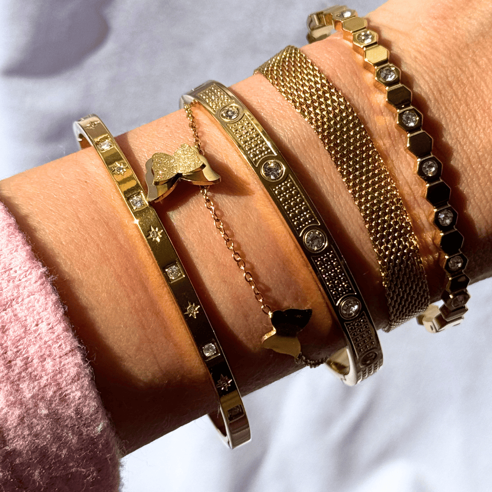 Close-up of a wrist wearing multiple gold bracelets on a light background