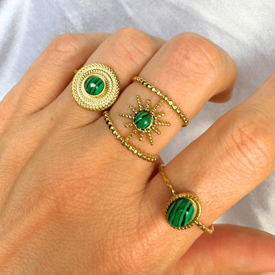 Gold rings with green gemstones on a hand against a white background