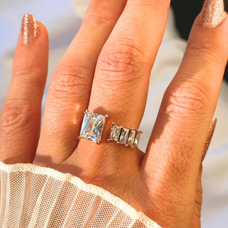 Hand wearing two gold rings with gemstones against a blurred background