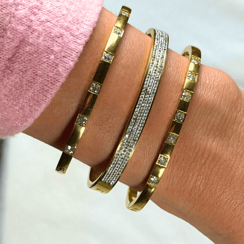Gold and diamond-studded bracelets on a wrist with a pink sleeve.