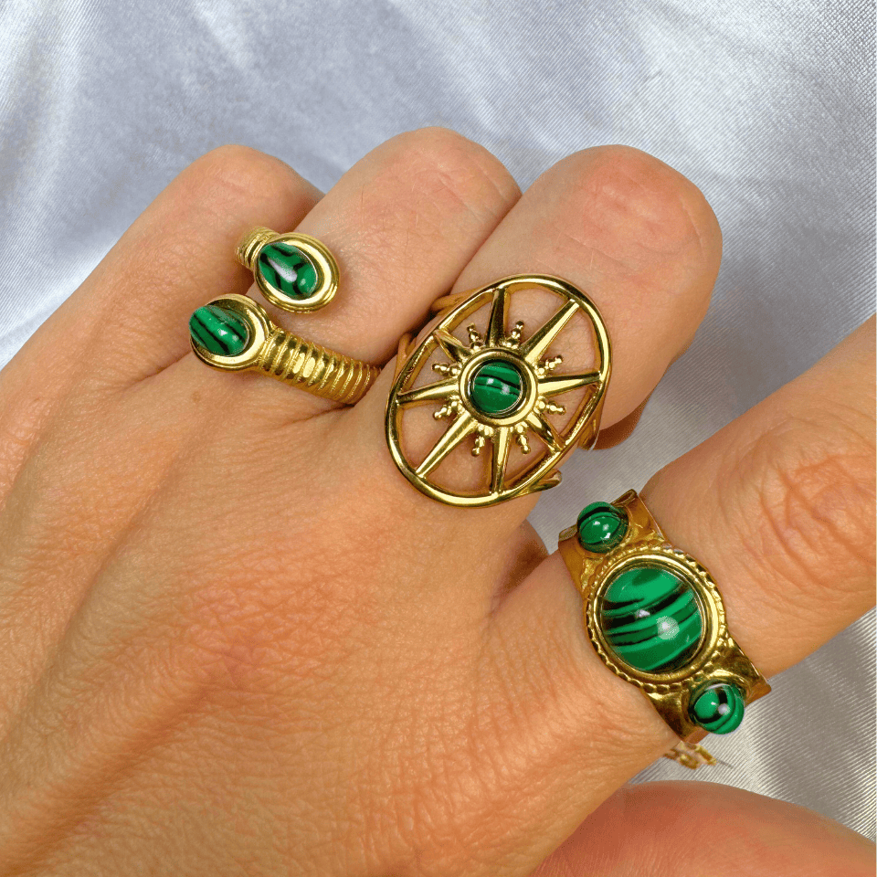 Gold rings with green gemstones on a hand against a light background