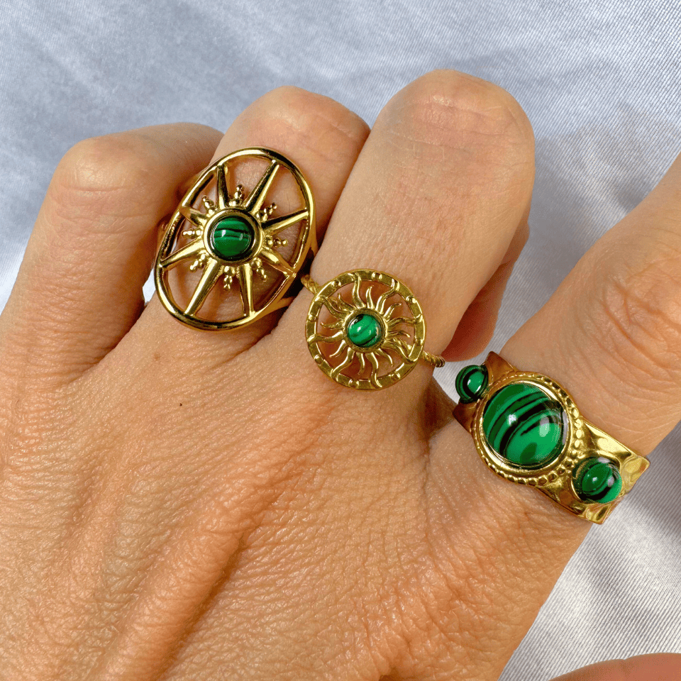 Gold rings with green gemstones on a hand against a light gray background