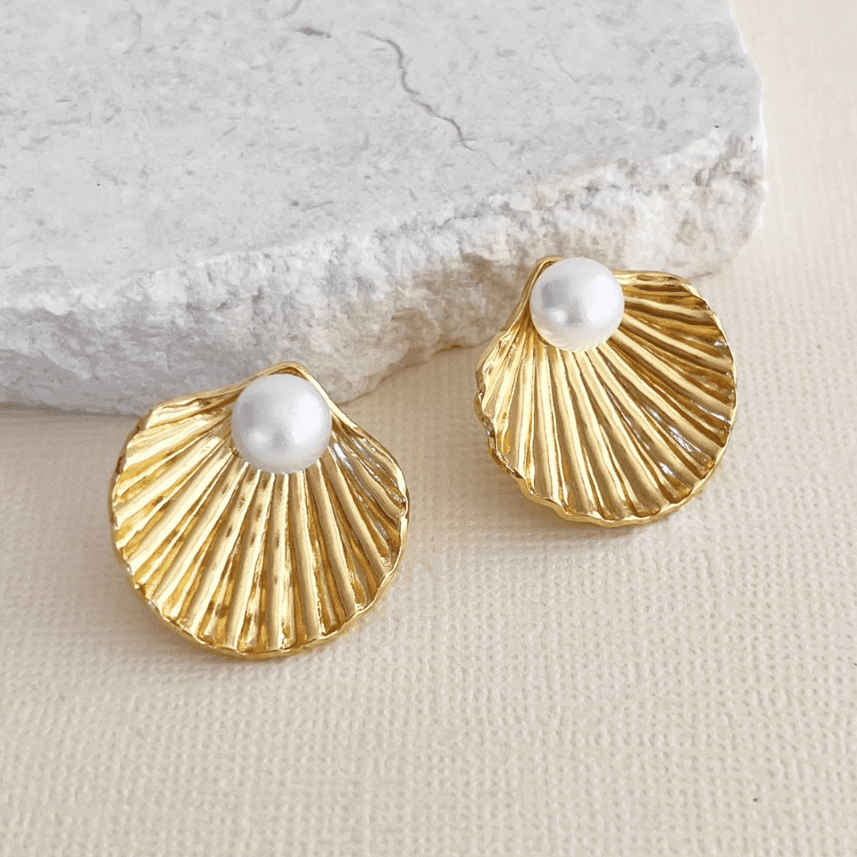 Gold shell-shaped earrings with pearls on a textured surface