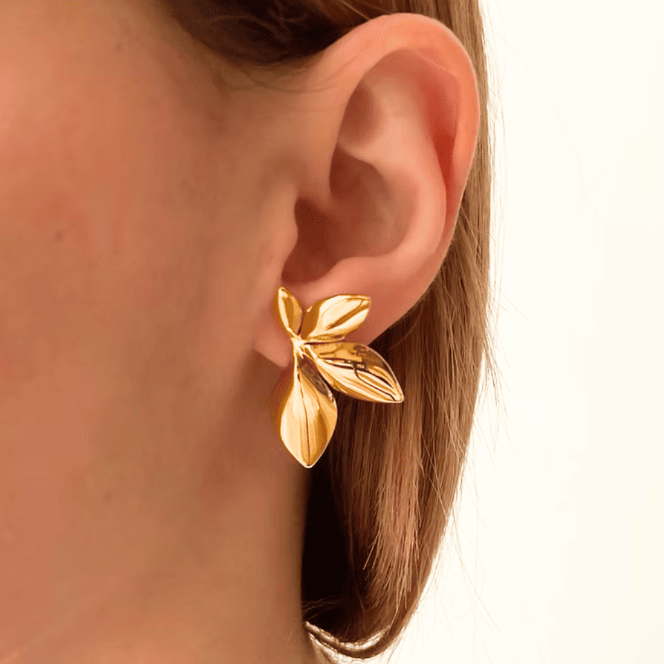Gold leaf earring worn by a person on a white background