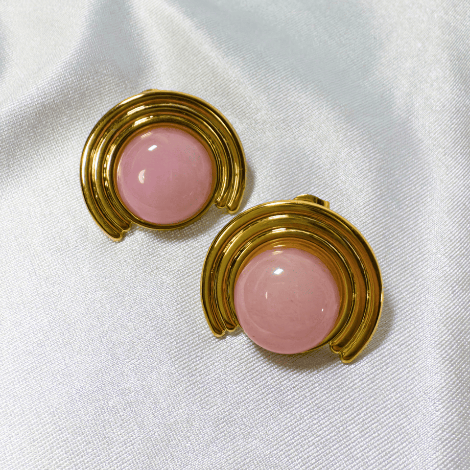 Pair of earrings with pink round stones and gold circular designs on a white fabric background