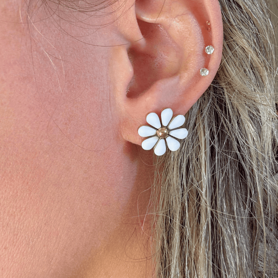 Close-up of an ear wearing a white flower-shaped earring with gold center.