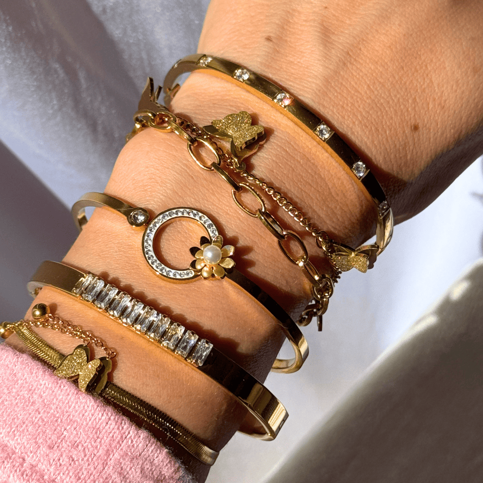 Close-up of a wrist wearing multiple gold bracelets with various designs.