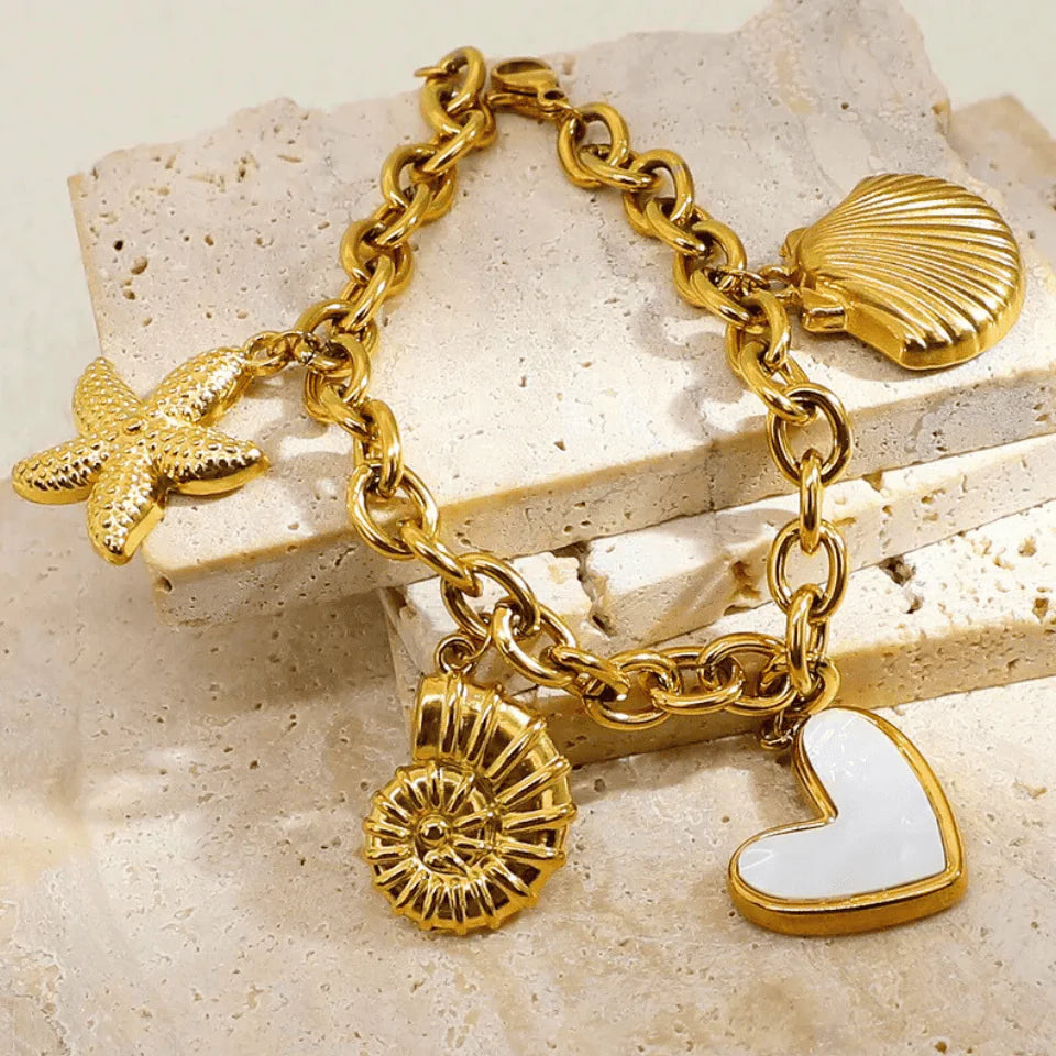 Gold charm bracelet with various charms on a beige stone surface