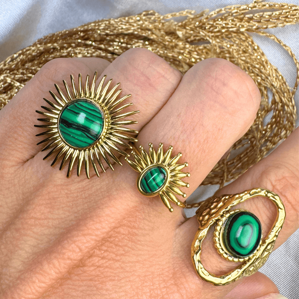 Gold rings with green gemstones on a hand, with gold thread in the background.