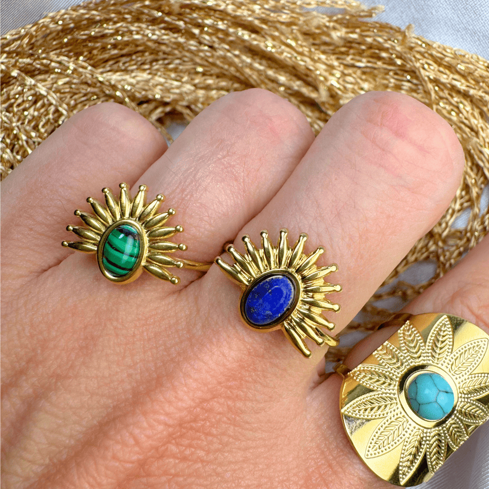 Gold rings with gemstones on a hand, with gold thread in the background