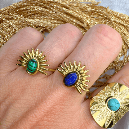Gold rings with gemstones on a hand, with gold thread in the background