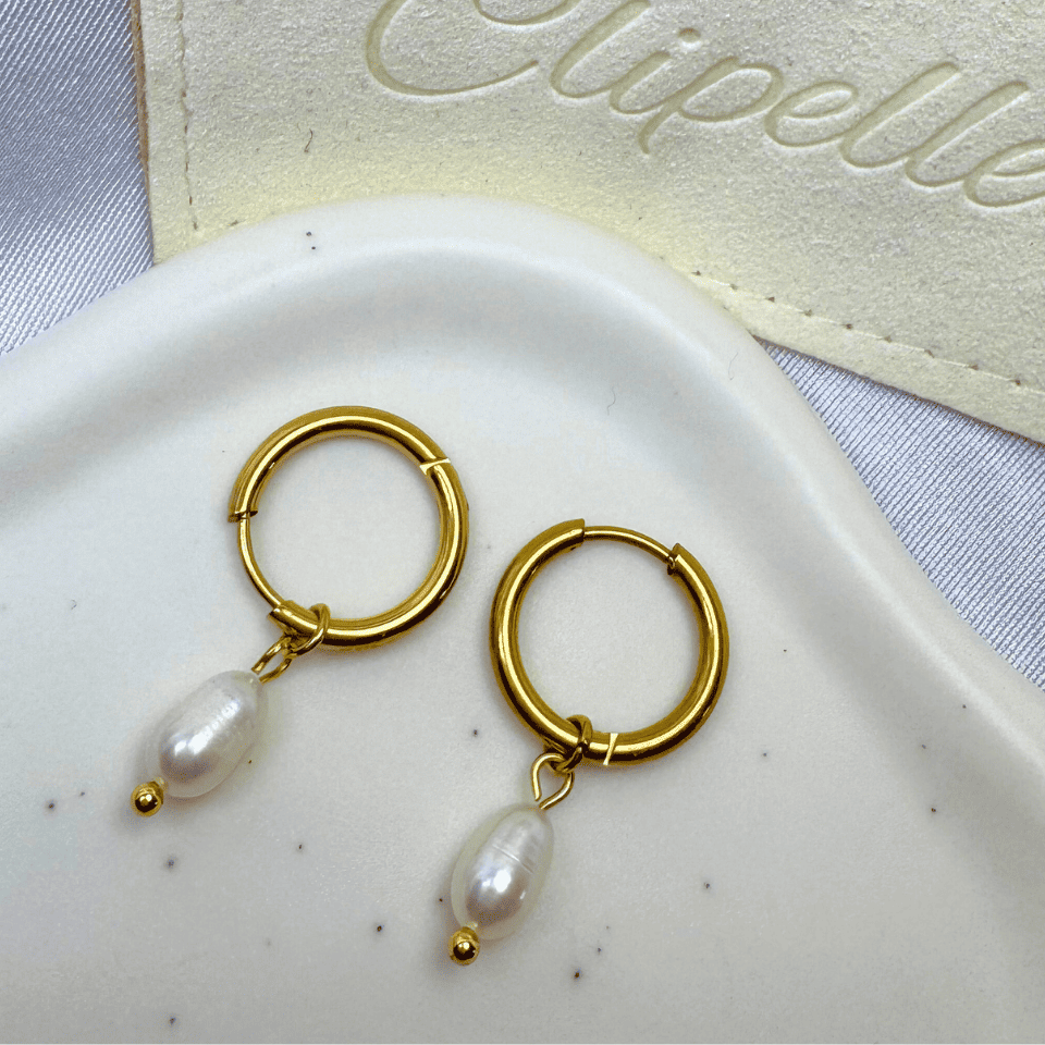 Gold hoop earrings with pearl drops on a white dish, with 'Elipelle' branding in the background.