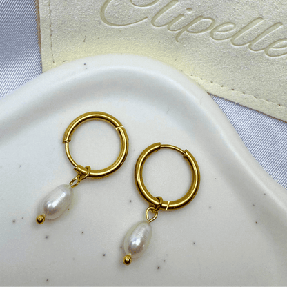 Gold hoop earrings with pearl drops on a white dish, with 'Elipelle' branding in the background.
