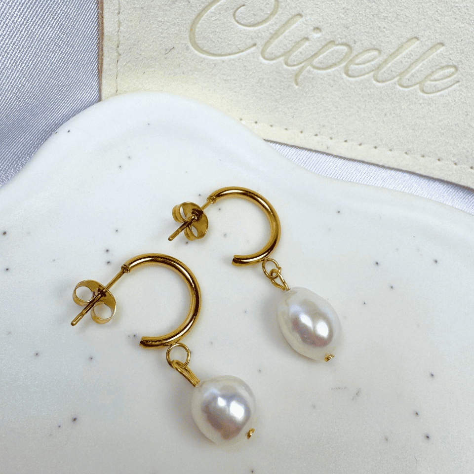 Gold earrings with pearls on a white surface with 'Elipelle' branding.