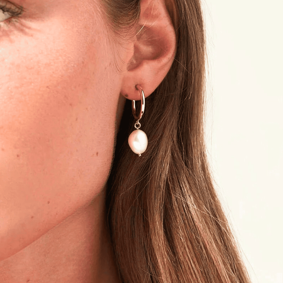 Close-up of a woman wearing a pearl earring with a plain background