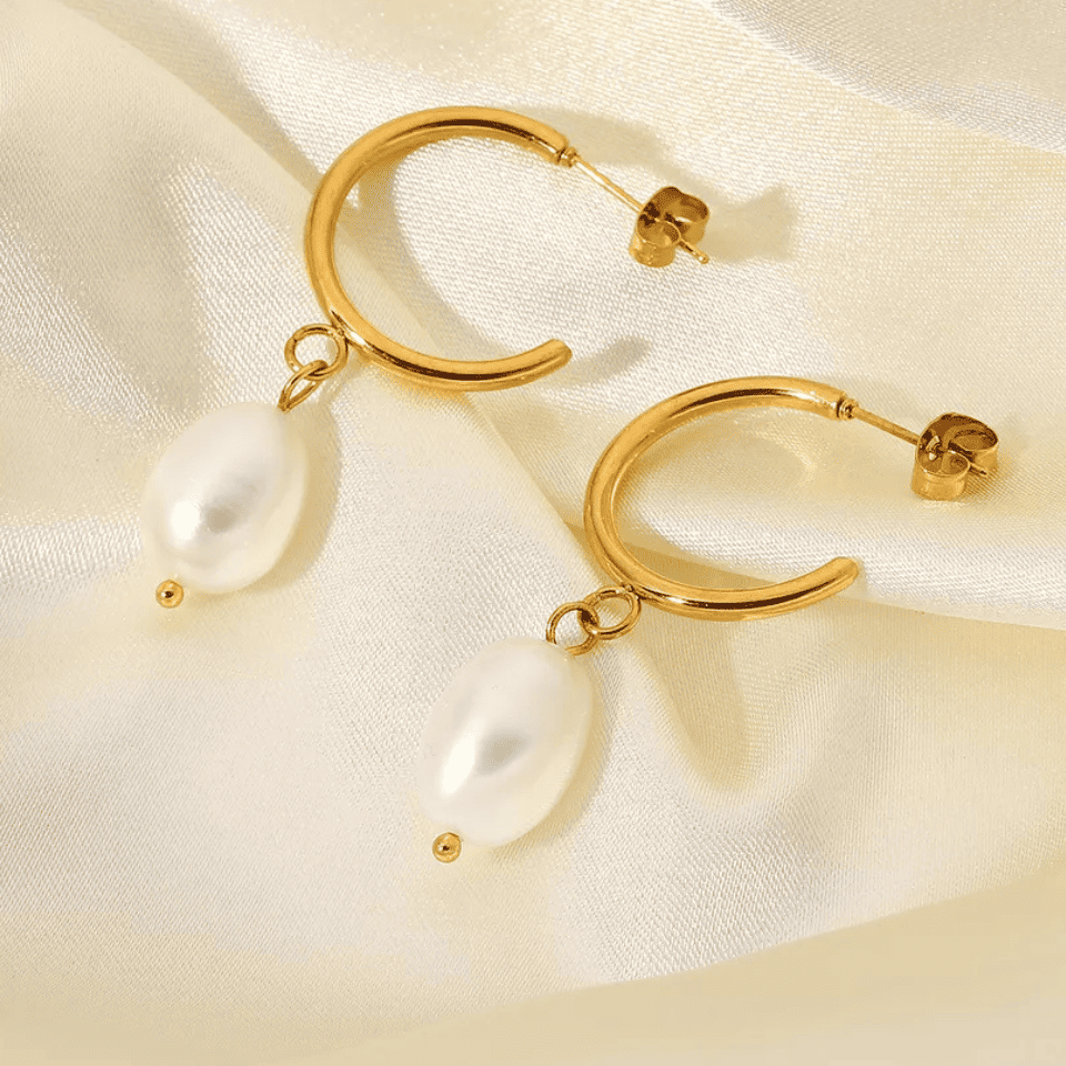 Gold hoop earrings with pearls on a beige fabric background