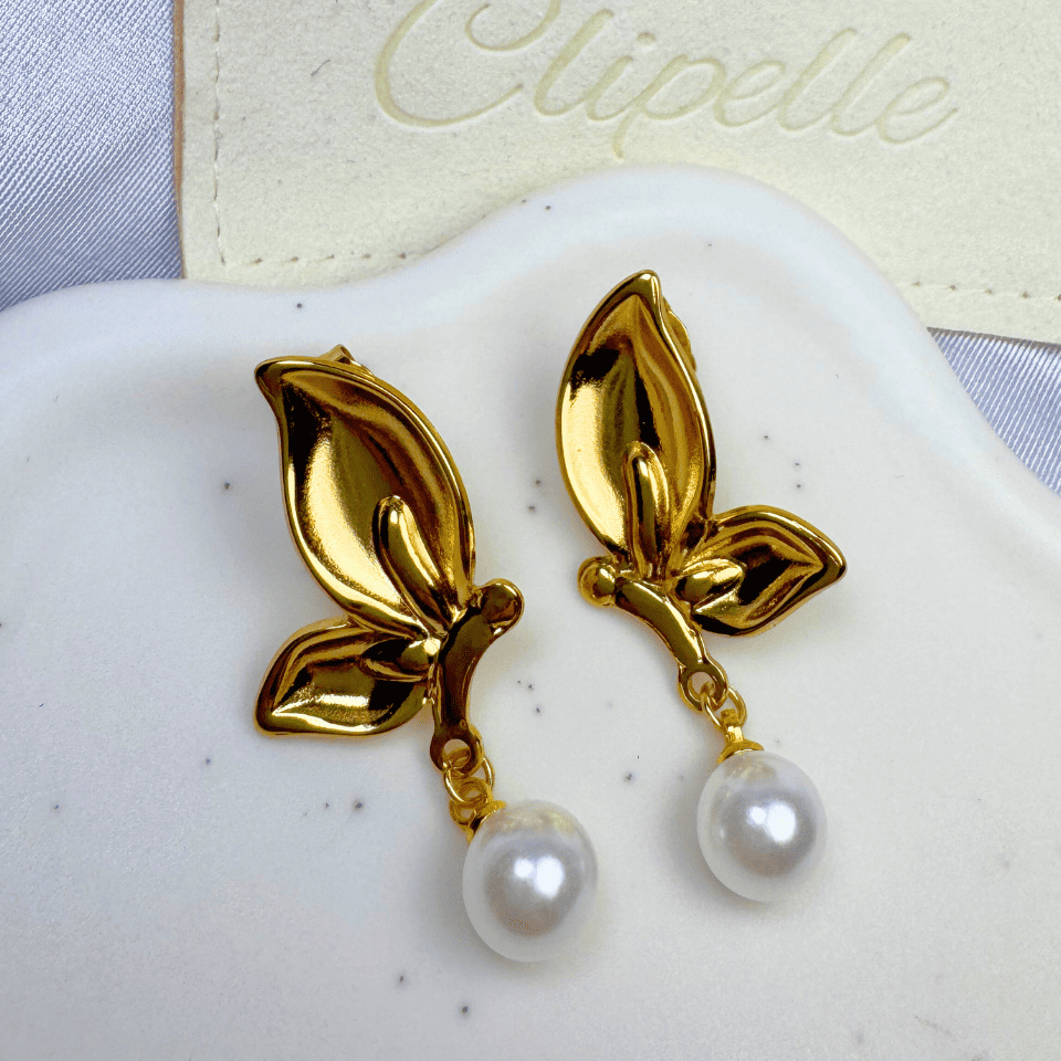 Gold leaf earrings with pearl drops on a white surface, branded 'Elipelle'.