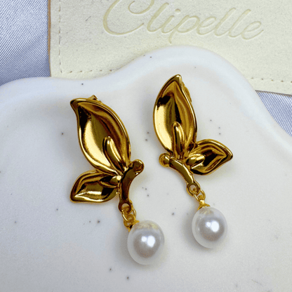 Gold leaf earrings with pearl drops on a white surface, branded 'Elipelle'.