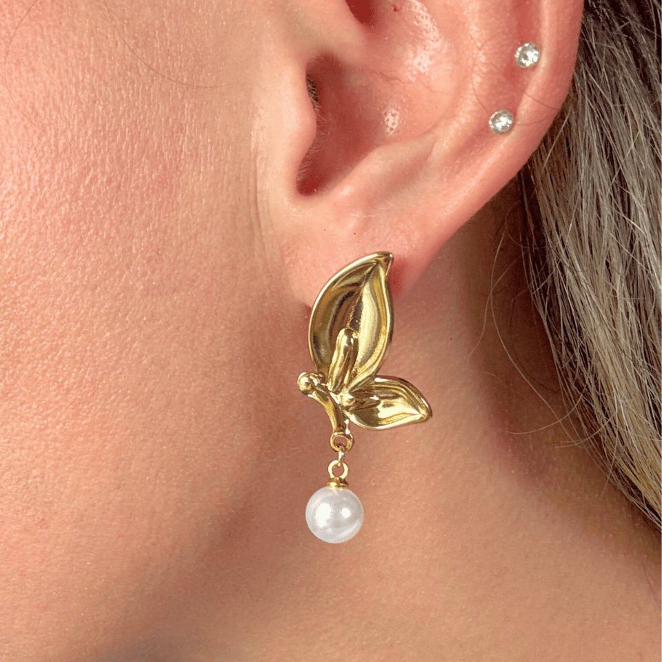 Gold leaf earring with a pearl drop worn by a person.