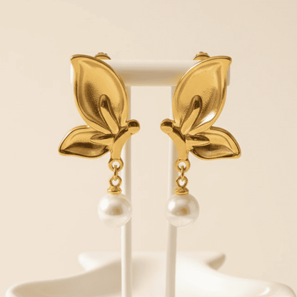 Gold leaf-shaped earrings with pearl drops on a beige background
