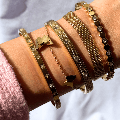 Close-up of a wrist wearing multiple gold bracelets on a light background