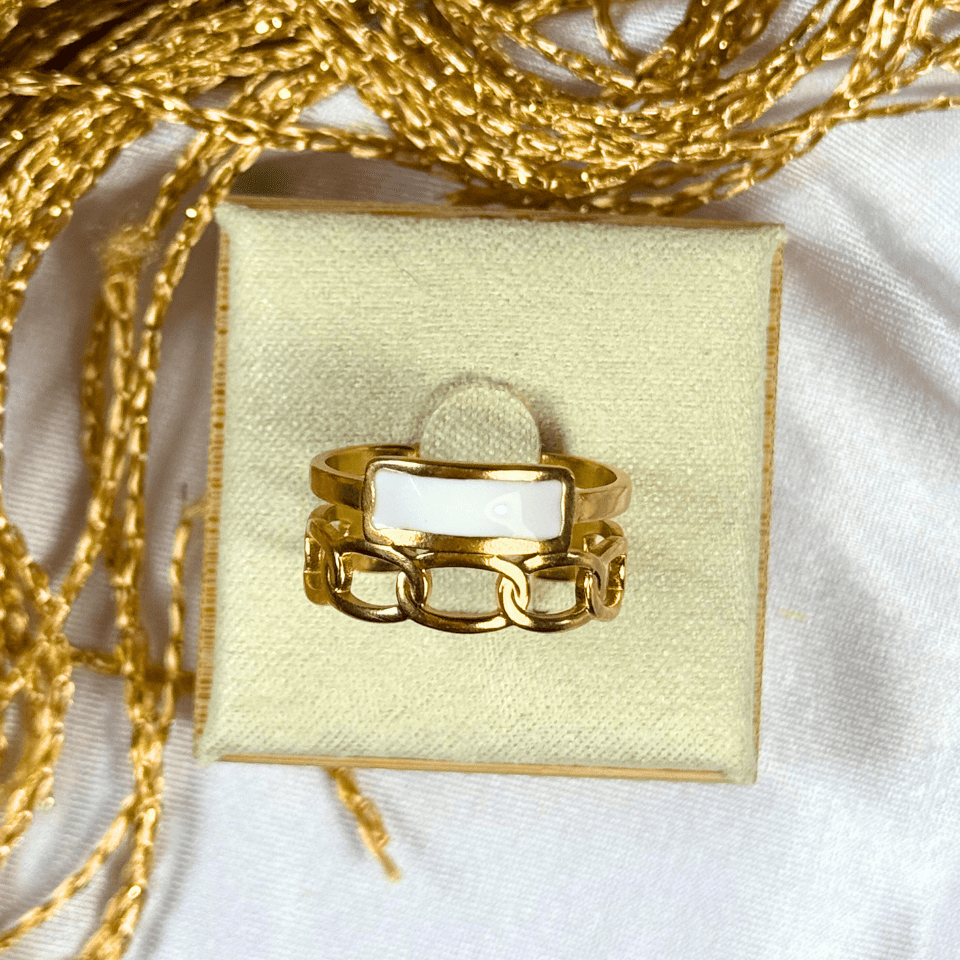 Gold ring with a white stone on a yellow cushion, surrounded by gold chains.