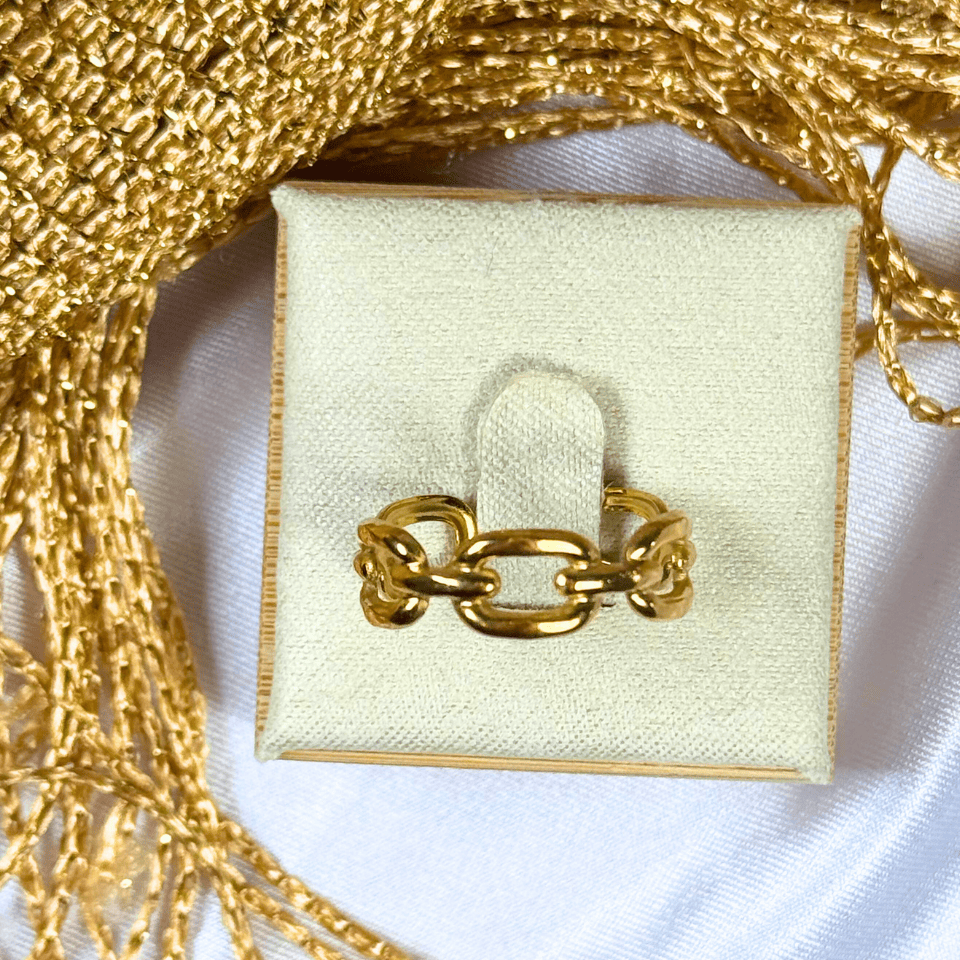 Gold chain ring on a white box with gold chains in the background