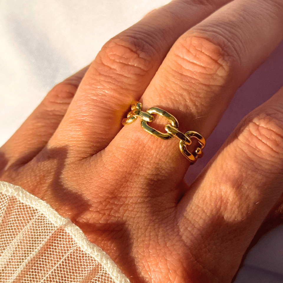 Gold chain ring on a person's finger with a blurred background