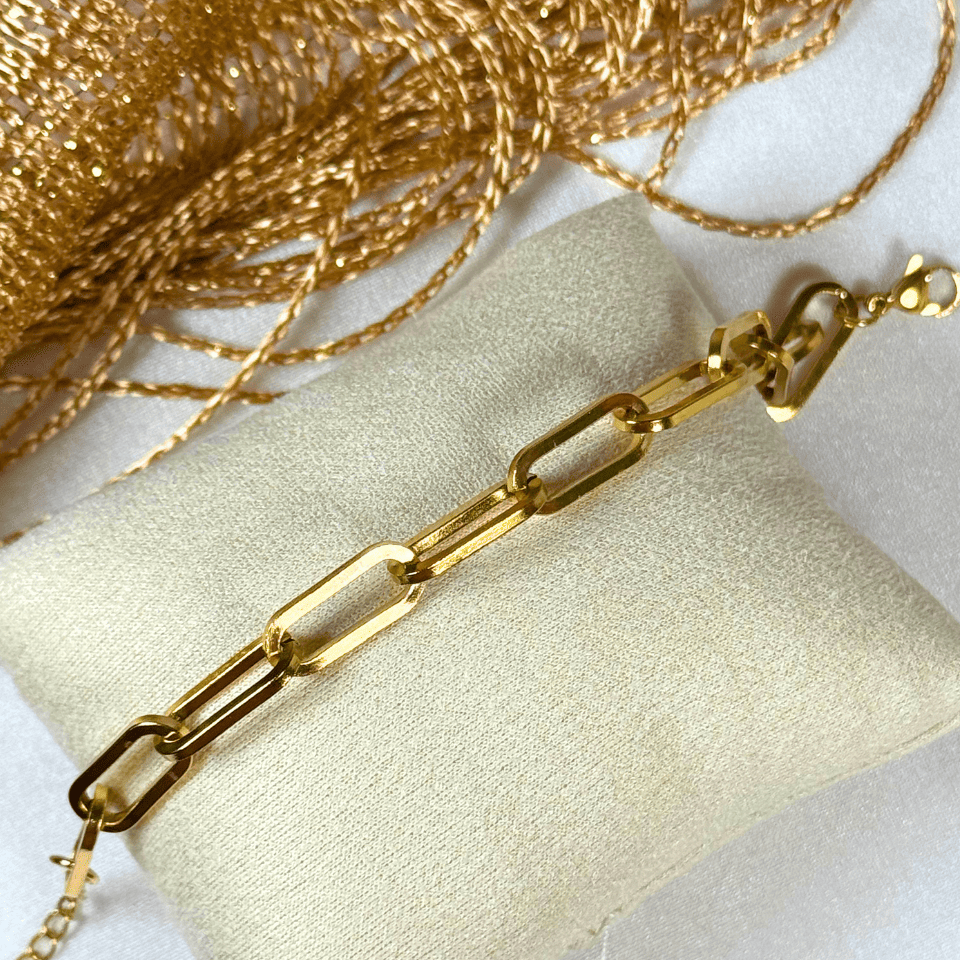 Gold chain necklace on a beige pillow with a white background