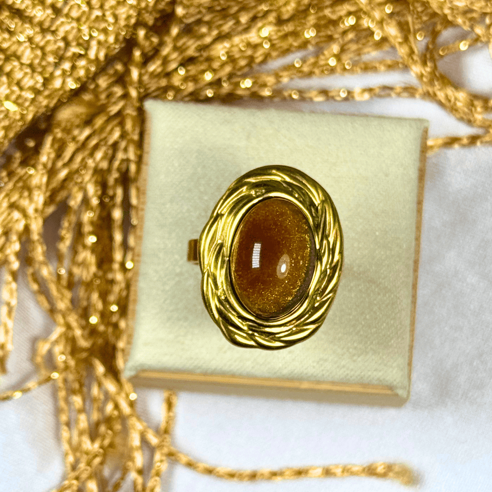Gold ring with a brown gemstone in a decorative box on a white background