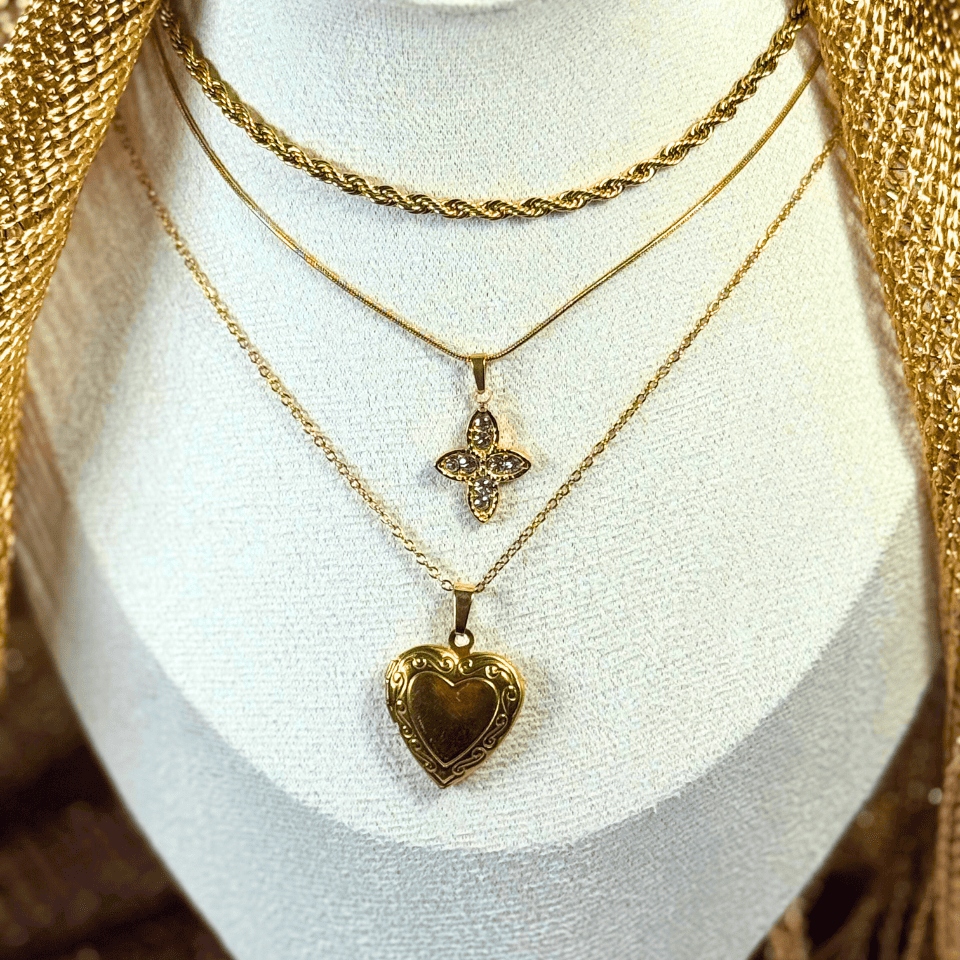 Three gold necklaces with pendants on a white stand