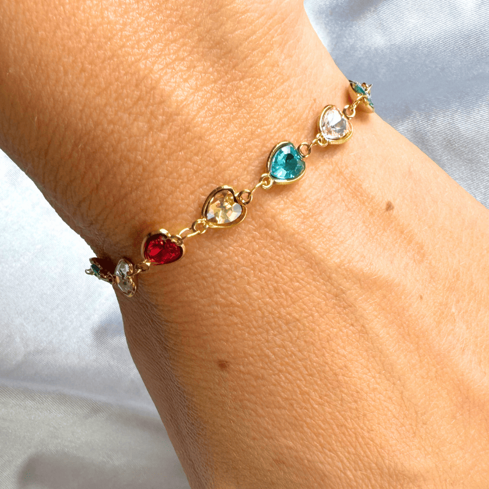Bracelet with colorful heart-shaped gemstones on a wrist against a light background