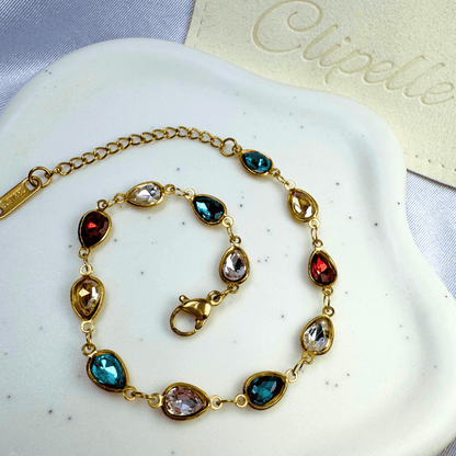Gold bracelet with colorful gemstones on a white stone surface with 'Clipette' branding.