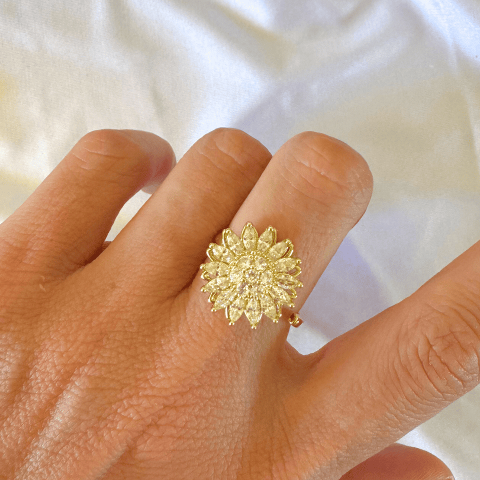 Gold ring with a sunflower design on a hand against a white background