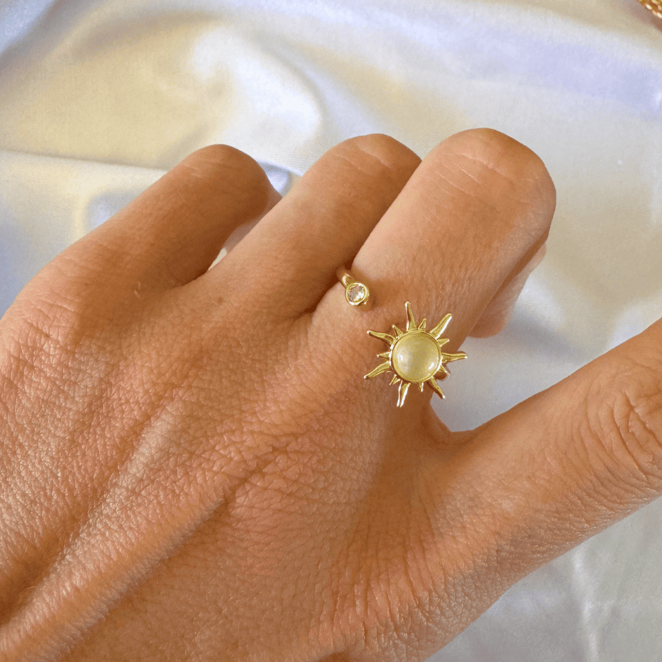 Gold ring with sun design on a hand against a white background
