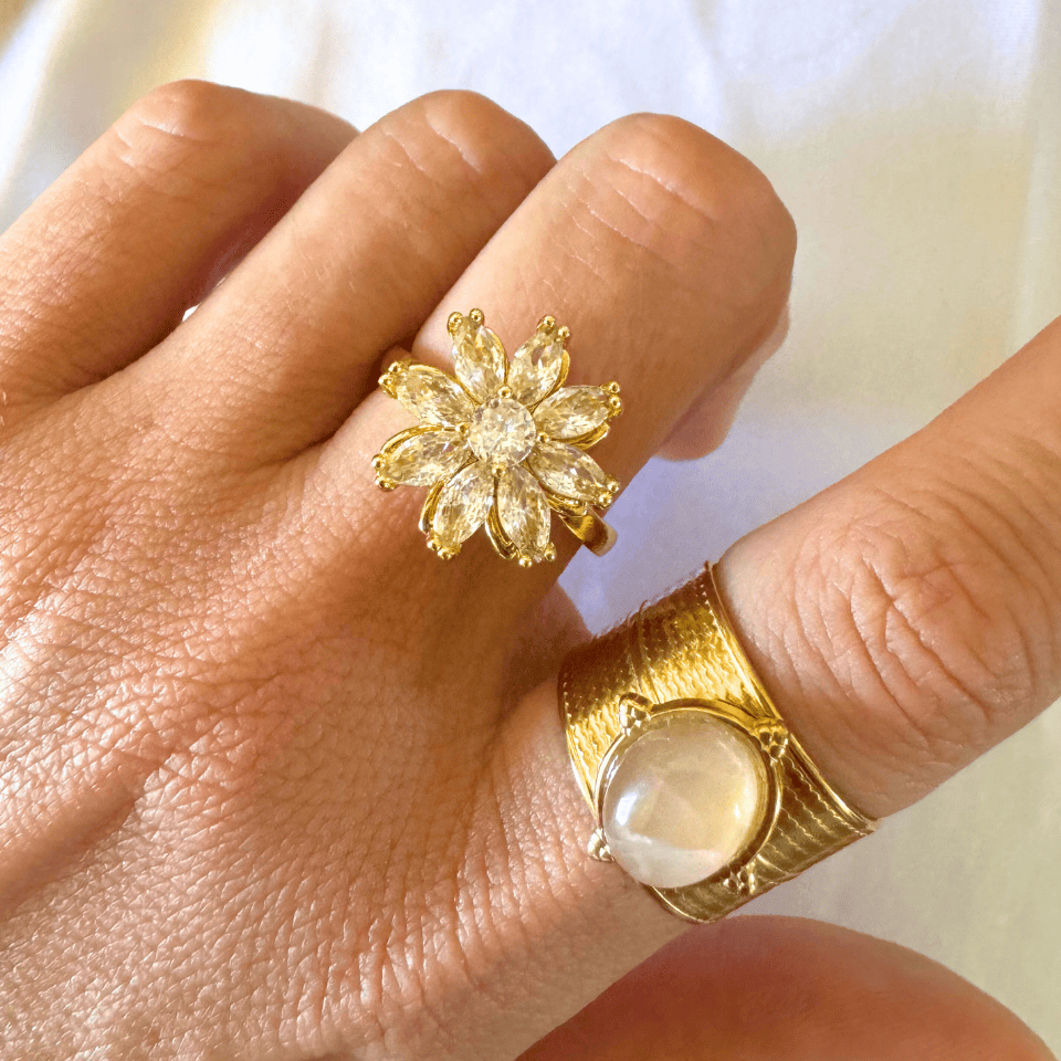 Gold ring with a floral design on a finger against a neutral background