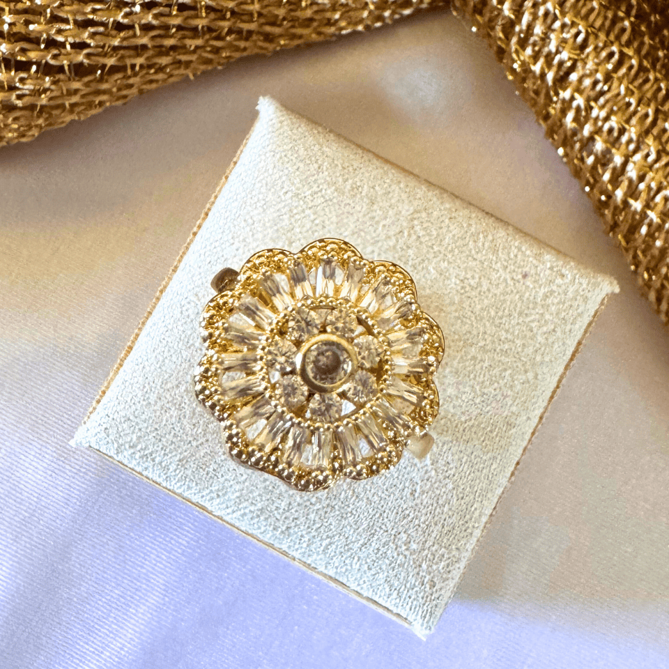 Gold floral brooch on a white box with gold ribbon