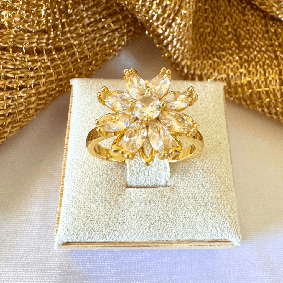 Gold flower-shaped ring on a white box with gold fabric background