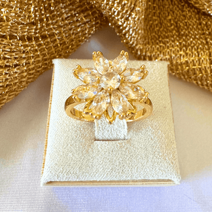 Gold flower-shaped ring on a white box with gold fabric background