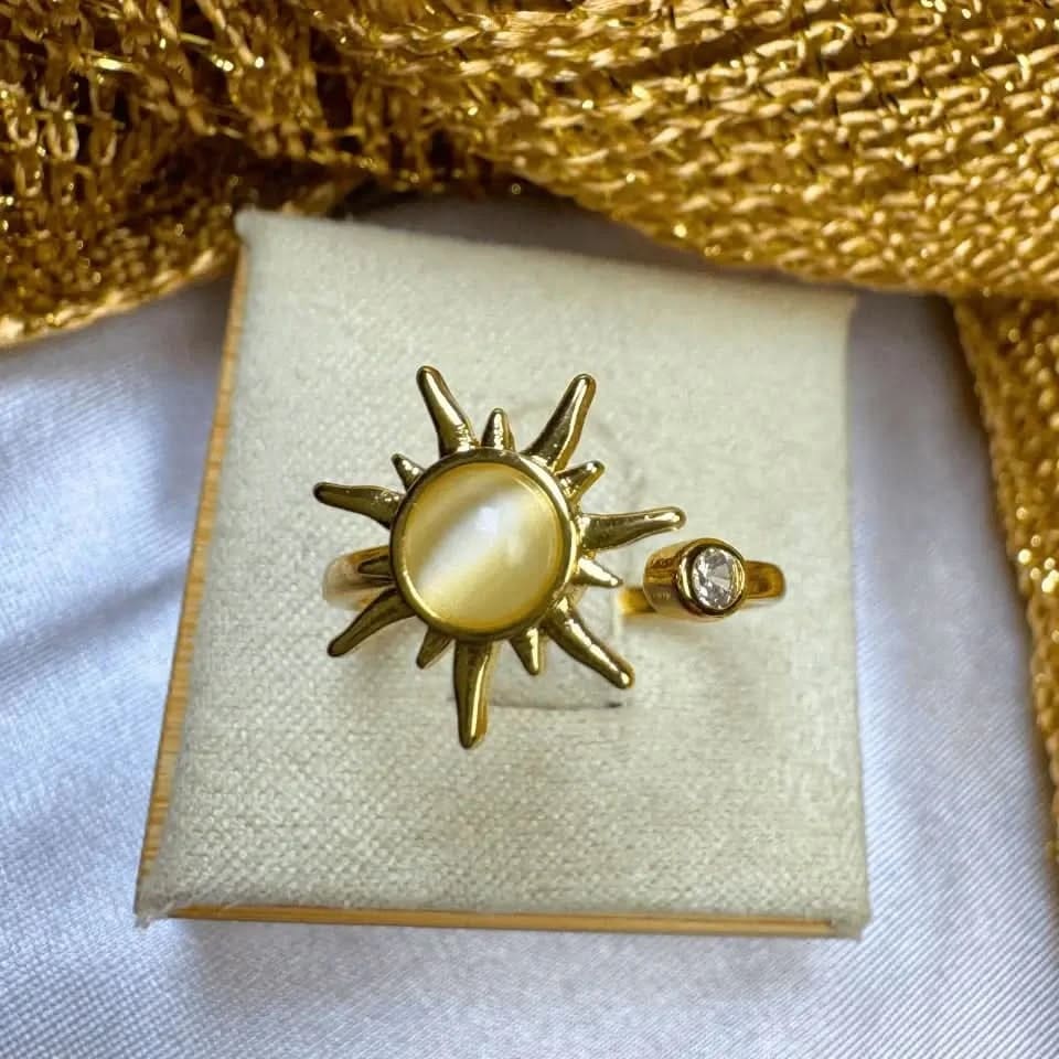 Gold sun-shaped ring with a central stone on a white box with gold fabric background