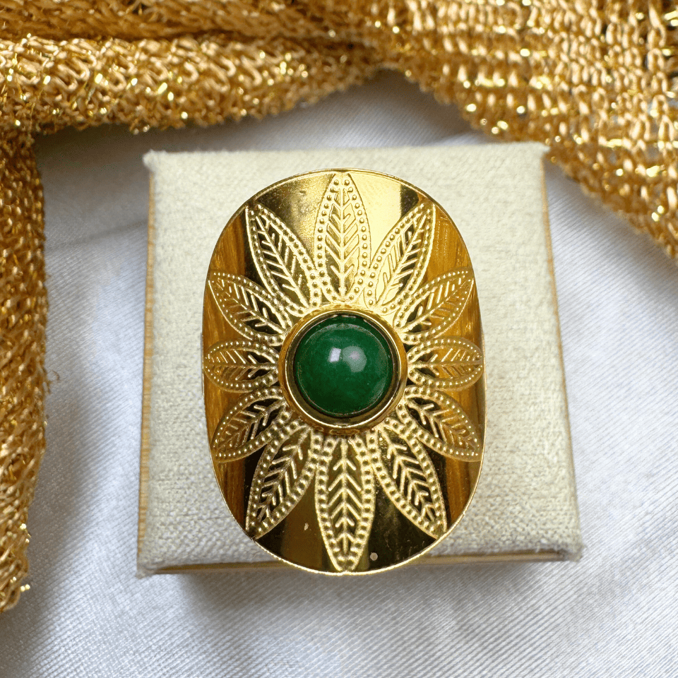 Gold brooch with green gemstone on a white cushion, gold fabric background