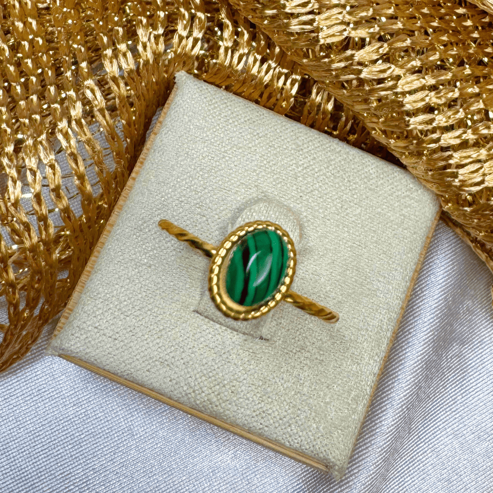 Gold ring with a green stone on a textured gold and white surface