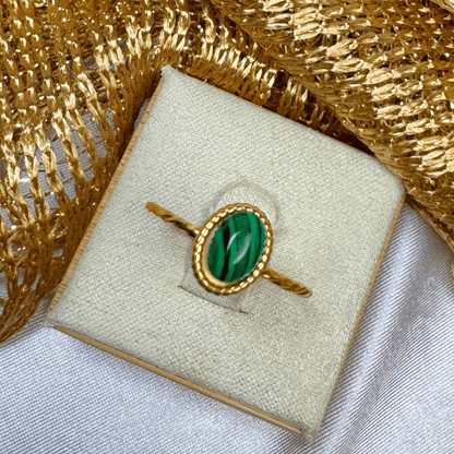 Gold ring with a green stone on a textured gold and white surface
