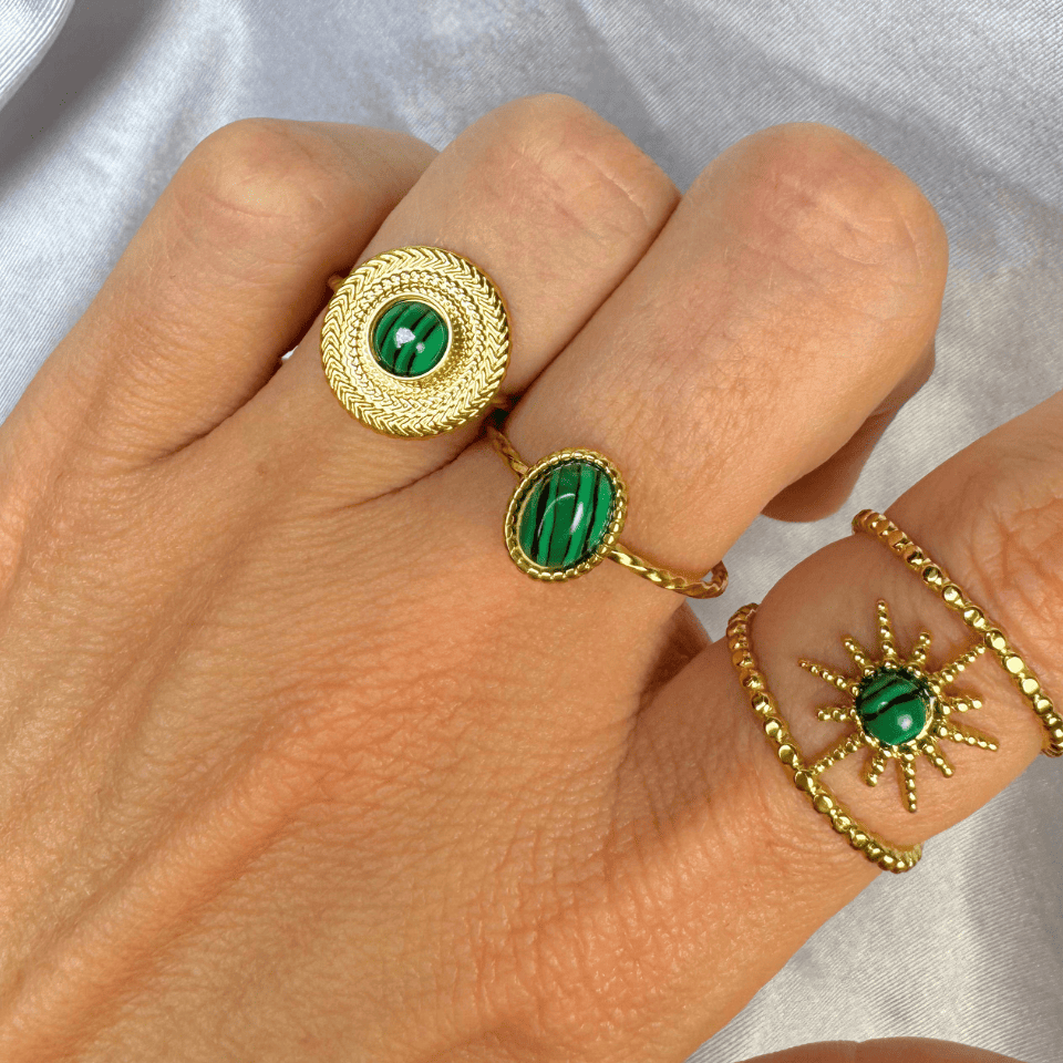 Hand wearing gold rings with green gemstones on a neutral background