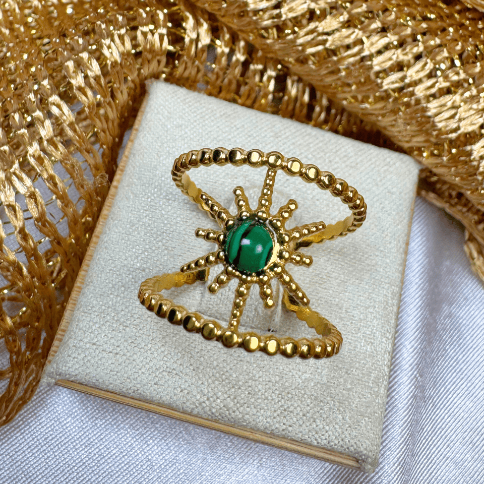 Gold ring with a green gemstone on a white box with gold decorative elements.