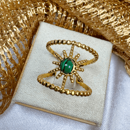 Gold ring with a green gemstone on a white box with gold decorative elements.