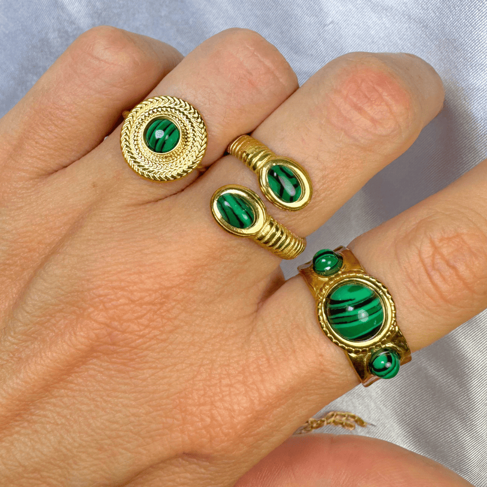 Gold rings with green gemstones on a hand against a neutral background