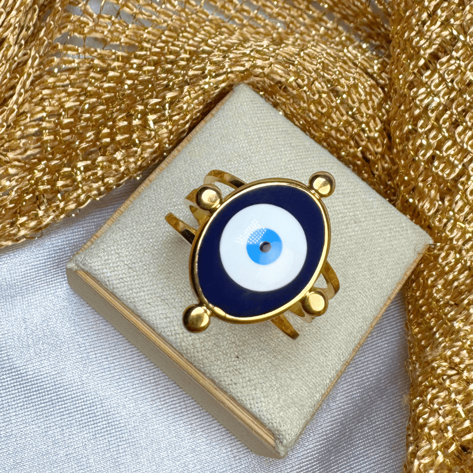 Gold ring with an eye design on a beige cushion against a gold textured background
