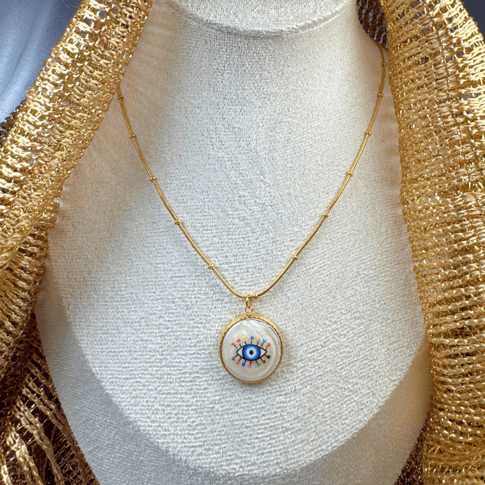 Gold necklace with an eye-shaped pendant on a mannequin bust.